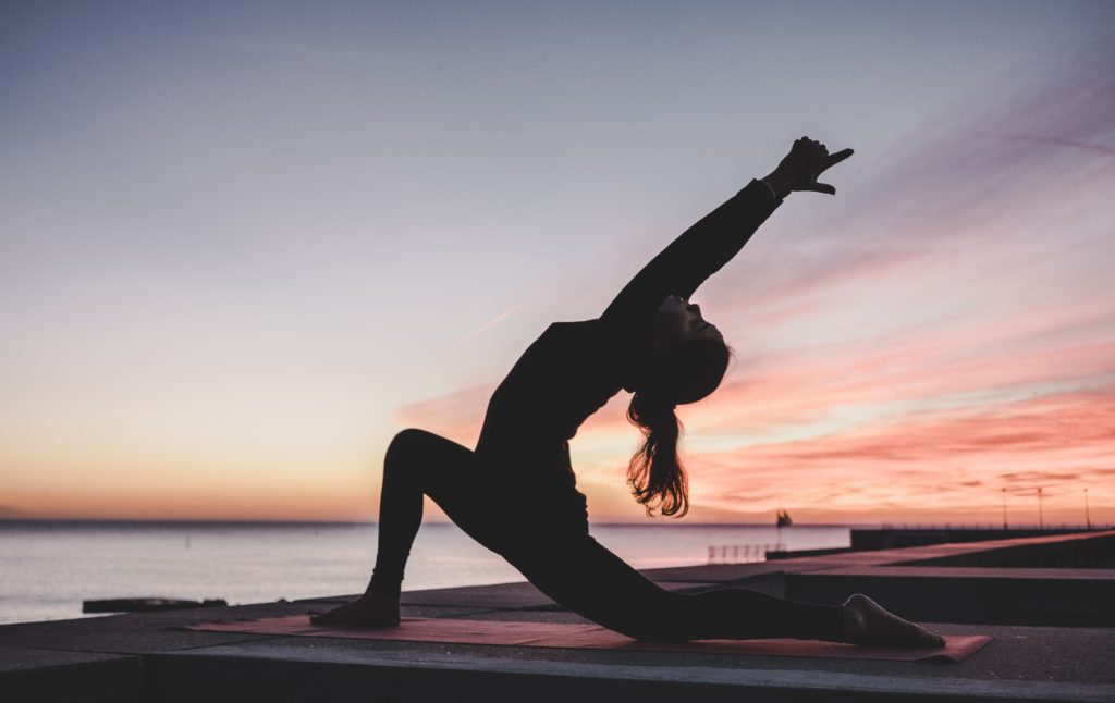 Woman practicing yoga on a mat, doing a deep lunge and stretching upward. 