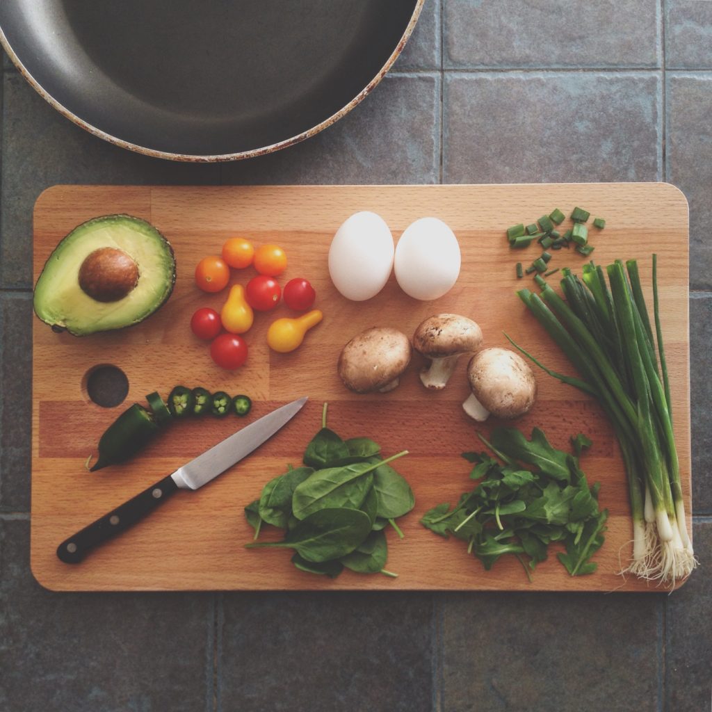 Cutting board with vegetables, avocado, spinach and green onion. Photo by Katie Smith on Unsplash