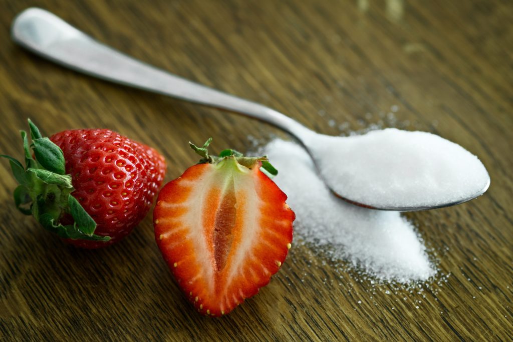 A spoonful of sugar on a table with cut strawberry on the side. Photo by mali maeder from Pexels