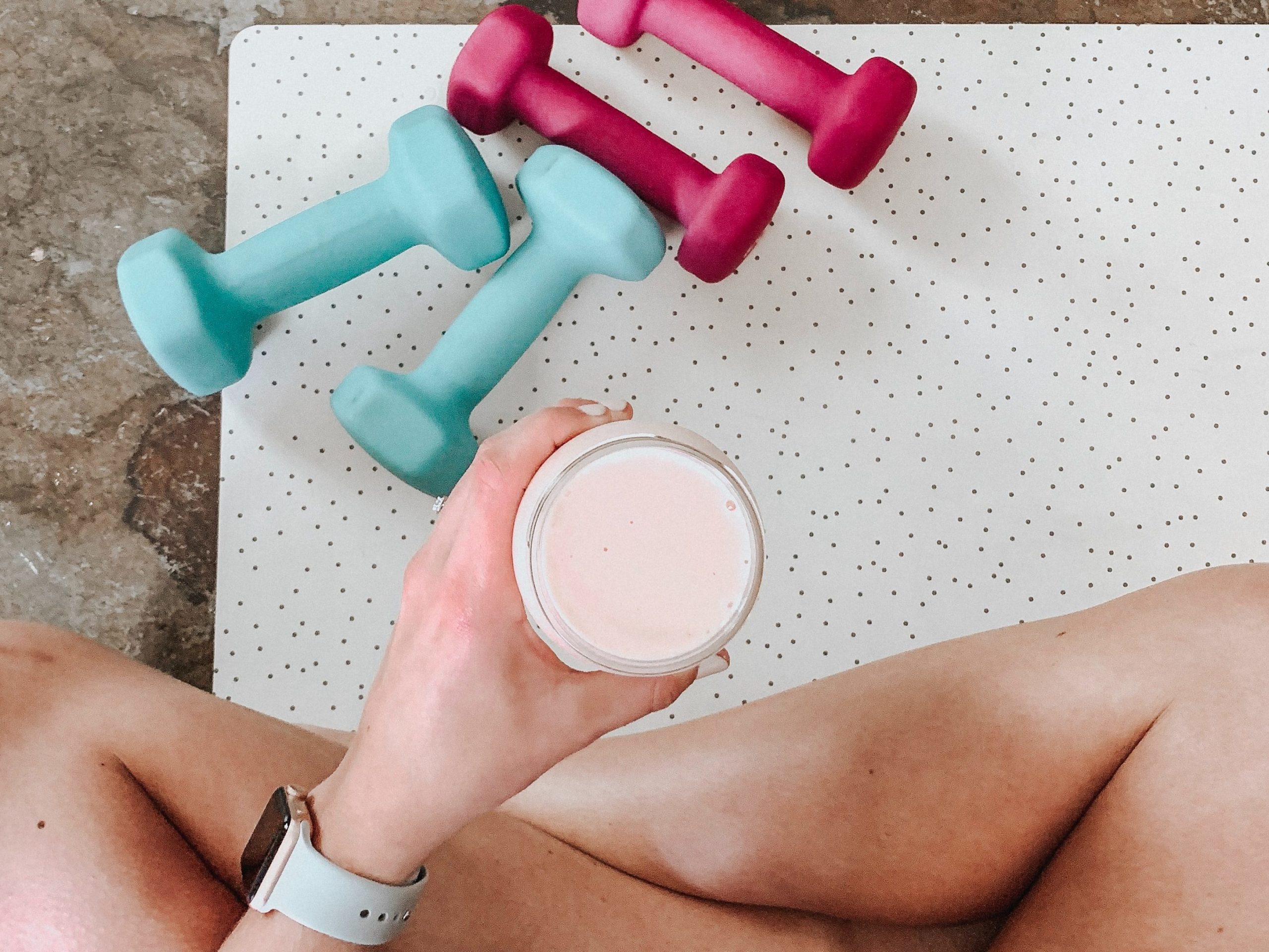 person holding smoothie on a yoga mat with weights.